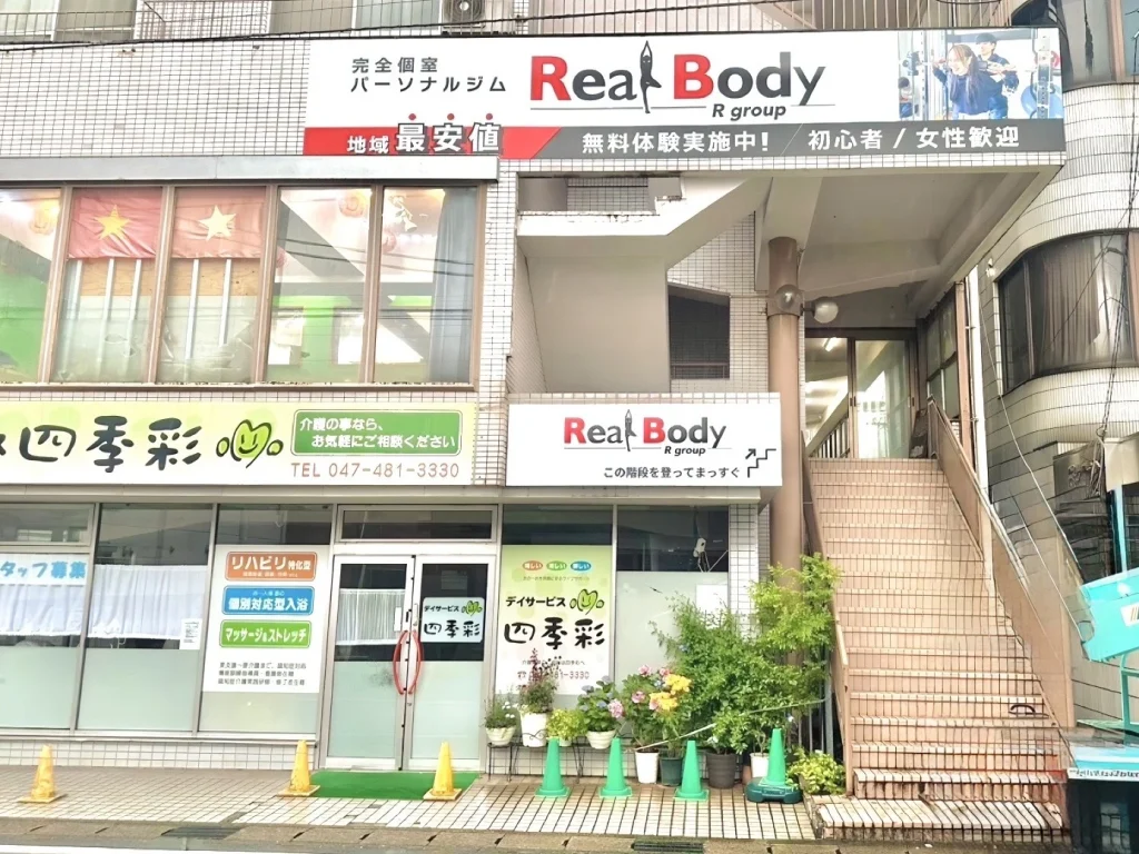 リアルボディ八千代台店の看板と、2階店舗へ向かう外階段